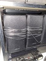 Three Denon rectangular speakers wrapped with wires, positioned horizontally.