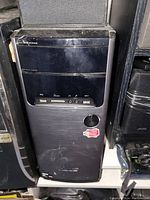 Front view of black desktop computer tower with visible USB ports, audio jacks, card reader slot, and sticker on front panel.