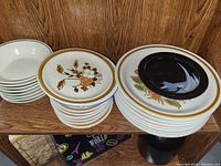 Multiple stacks of ceramic dishware including bowls and plates, some with floral patterns and others plain with colored rims, all vintage style.