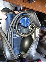 Photo showing the blood pressure monitor gauge, cuff, and hand pump inside an open black zippered leather case.