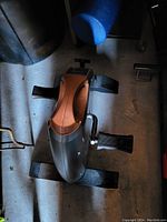 Full view of the leg exercise machine showing black and brown plastic housing, foot pedals, and base.