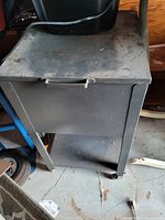 Closed metal file cabinet showing the worn and dusty top surface and the legs with wheels.