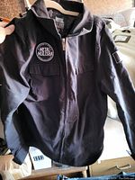 Front view of black Metal Mulisha jacket showing patch, zipper, and pocket details.