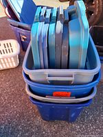 Image showing a stack of multiple blue plastic lids inside a blue plastic tote bin outdoors.