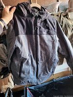 Front view of a two-tone jacket in gray and dark gray with hood, zipper, and pockets.