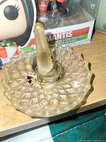 Photo of a clear textured glass ring holder with a diamond-patterned dish base and central cone, holding several rings of unknown metal.