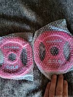 Two pink 2.5 lb Body Rock weight plates wrapped in bubble wrap on a dark fabric background.