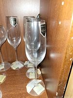 Three crystal wine glasses with Leonardo labels photographed inside a wooden cabinet.