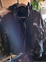 Front view of black The North Face jacket with hood and embroidered logo on chest.