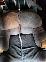 Single image showing one silver metal curl bar weight bar resting on a brown cushioned chair. The bar has black rubber grips on both ends and a slight zigzag shape in the middle.