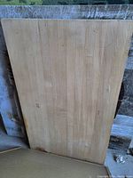 Photo showing a rectangular solid wooden board made of light-colored wood with visible grain patterns and minor blemishes along edges
