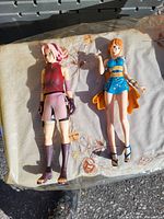 Two anime action figures placed on outdoor surface, showing full body from head to foot: Sakura Haruno on left and Nami on right.