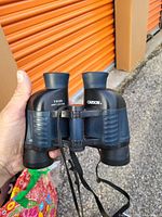 Close-up photo of black Carson binoculars with 7x35 magnification markings, showing textured grips and attached neck strap.