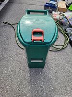 Closed green plastic compost bin with visible red foot pedal on lid, showing top and front view.