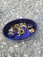 Open container showing various pairs of earrings in mixed metals and styles resting on purple fabric lining.