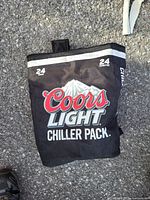 Photo of the black Coors Light Chiller Pack cooler bag outdoors on a paved ground, showing front logo and capacity details.
