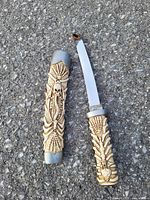 Photo showing a decorative dagger with an intricately carved bone handle and sheath with skull motifs, the blade is curved metal.