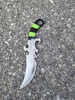 Dagger lying on asphalt ground showing full length with serrated edge and paracord wrapped handle