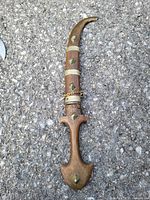 Dagger in closed scabbard showing wooden handle with metal studs and chain.