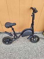 Side view of black compact electric bike showing frame, saddle, tires, and pedals.