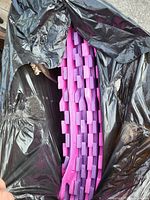 Partial view of pink foam mats inside a black garbage bag, showing the interlocking edges and textured surface.