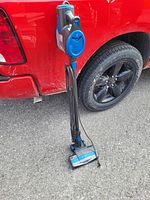 Full view of the Shark Rocket handheld vacuum standing upright with attached nozzle next to a red truck.