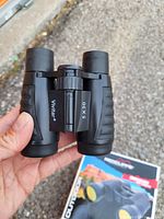 Photo showing front view of compact black Vivitar binoculars labelled 5x30 with textured grips and central focusing wheel.