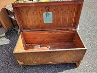 View of open wooden storage trunk showing interior lined with wood and metal lock plate inside lid.