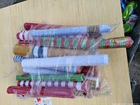 Multiple assorted rolls of gift wrapping paper in various colors and holiday-themed patterns wrapped together in plastic on a wooden surface.