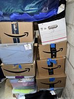 Photo showing stacked cardboard Amazon boxes and plastic bins filled with fabric pieces, held together with blue tape.