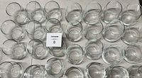 Top down view of approximately 50 clear glass drinking glasses arranged closely in rows, showing various sizes of plain glassware.