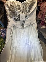 Front view of the white strapless wedding dress showing the silver sequin floral embellishments on the bodice, size tag 2 attached.