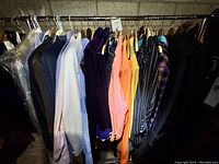 Wide view of multiple men's theater costumes on hangers, showing variety of jackets and shirts in different colors and materials.