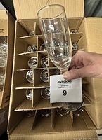 Box holding approximately 20 clear glass wine glasses with dividers for separation. Hand holding one glass for scale.
