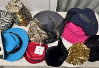 Overview of 8 women's hats in various styles and colors on a table including patterned, felt, sequined, and feathered hats.