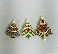 Front view of 3 gold-tone Christmas tree brooches decorated with red, green, blue, and clear rhinestones on gray background
