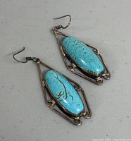 Close view of turquoise drop earrings showing call hook attachments and silver scroll frame.