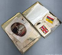 Open metal box containing multiple stacks of silk cigarette cards with various designs including flags and portraits