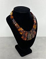 Front angle view of the necklace on black stand showing individual trapezoidal Bakelite pieces and central floral carving.