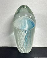 Front view of clear glass paperweight featuring blue and white jellyfish inside, shaped with rounded top