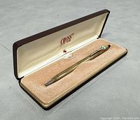 Open pen case with gold tone pen placed on beige velvet cushion inside cream satin lining