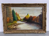 Framed landscape oil painting showing river, trees in autumn colors and carved wooden frame.