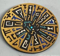 Front of the brooch showing detailed geometric enamel design in black, blue, white, and turquoise on gold-tone surface.