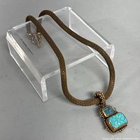 Full view of bronze necklace with toggle clasp and pendant featuring turquoise and blue stones displayed on clear stand.