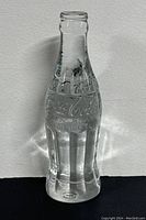 Clear lead crystal Coca-Cola bottle on white background showing front and embossed logo details.
