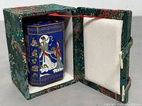 Octagonal cloisonne enamel canister inside original decorative fabric box with white padding.