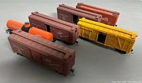 Six HO scale train cars on display including four brown boxcars, one yellow boxcar, and one orange tanker car.