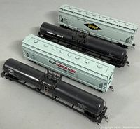 Four miniature train cars displayed outside of their boxes: two white hopper cars with Dow and ACP Center Flow branding, two black tank cars including Canadian Pacific.