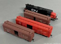 Four HO scale miniature trains, including 1 CN locomotive and 3 boxcars (2 Canadian Pacific brown, 1 Great Northern red) lined up closely in a group.