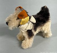 Side front view of plush Airedale Terrier showing tag and white ribbon collar with bell.
